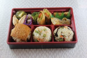 ▼「ガッツリ系」のお弁当。主菜は、さつまいもの肉巻きと鱈(たら)のムニエル。 地元野菜が10種類ほど使われています。